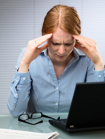 A stressed young business woman looks down and massages her head at her workplace.