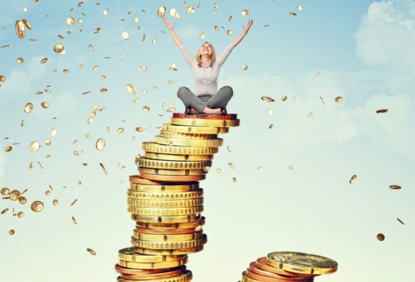 Kvinde sidder ovenpå en høj stak overdimisioneret mønter og jubler med armene over hovedet