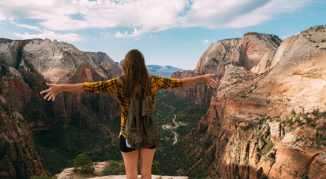 Kvinde står ved kæmpe bjergkæde og kigger ud over kløft med armene ud til siden med en følelse af frihed