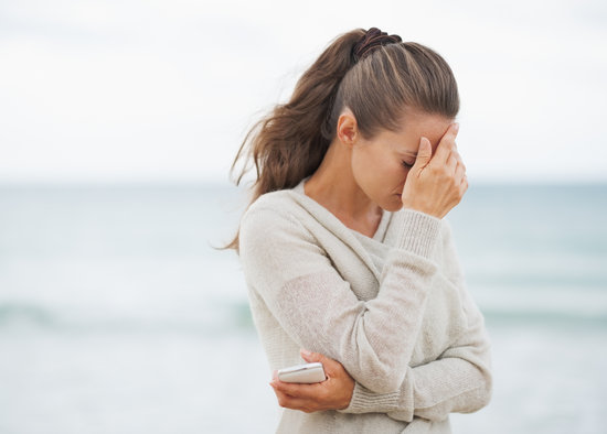 Stressed young woman in sweater on beach with cell phone